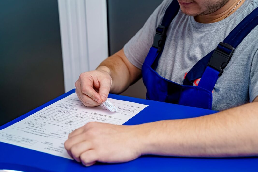 Tradesperson reviewing paperwork and invoices at a desk Mechanic in overalls reviewing paperwork and invoices at an office desk